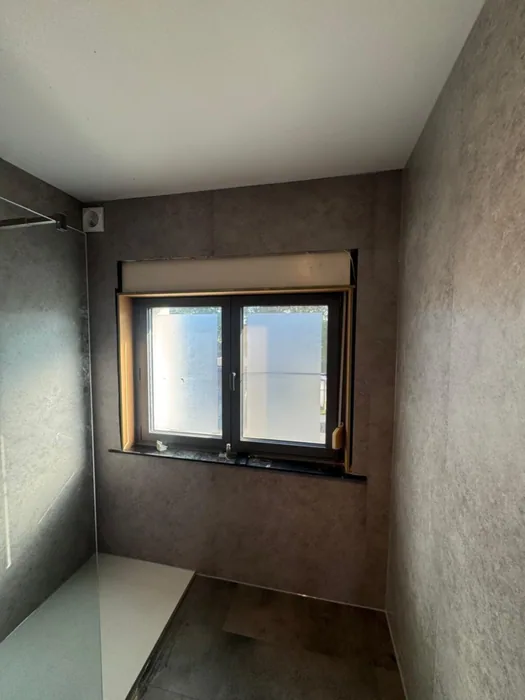 Badkamer rondom bekleed met grijze stenenlook wandpanelen, raam en inloopdouche met witte douchebak